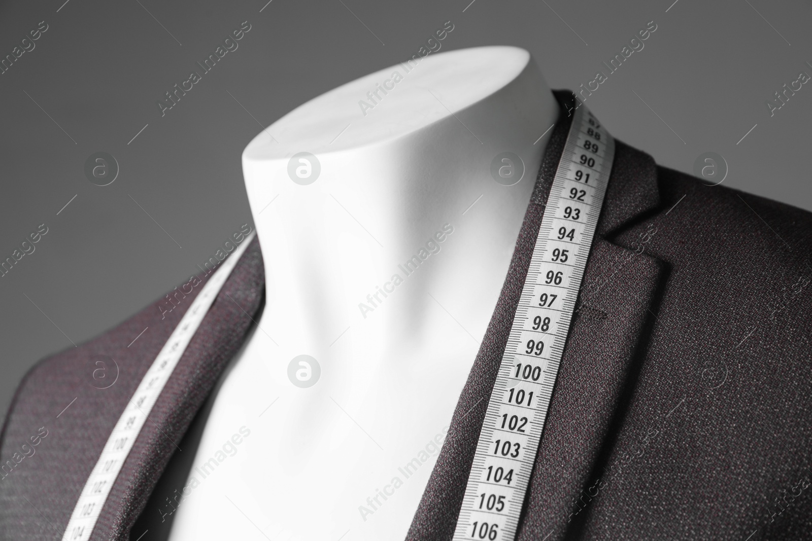 Photo of Male mannequin with brown jacket and measuring tape on grey background, closeup