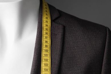 Male mannequin with brown jacket and measuring tape on grey background, closeup