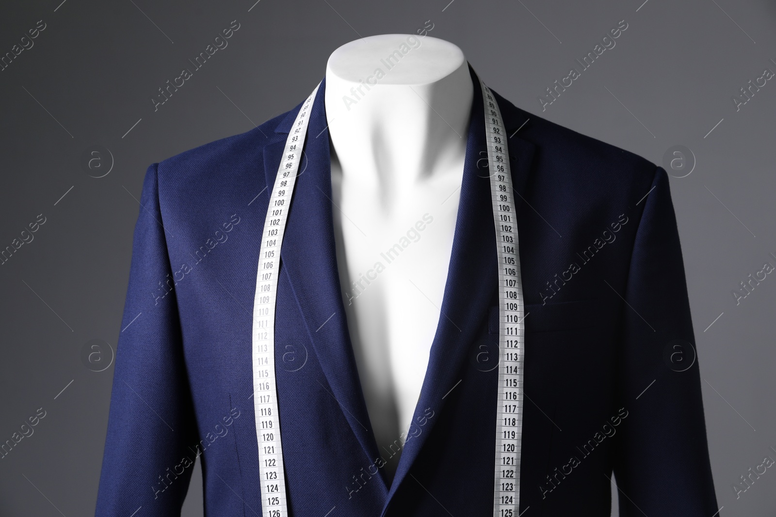 Photo of Male mannequin with blue jacket and measuring tape on grey background, closeup