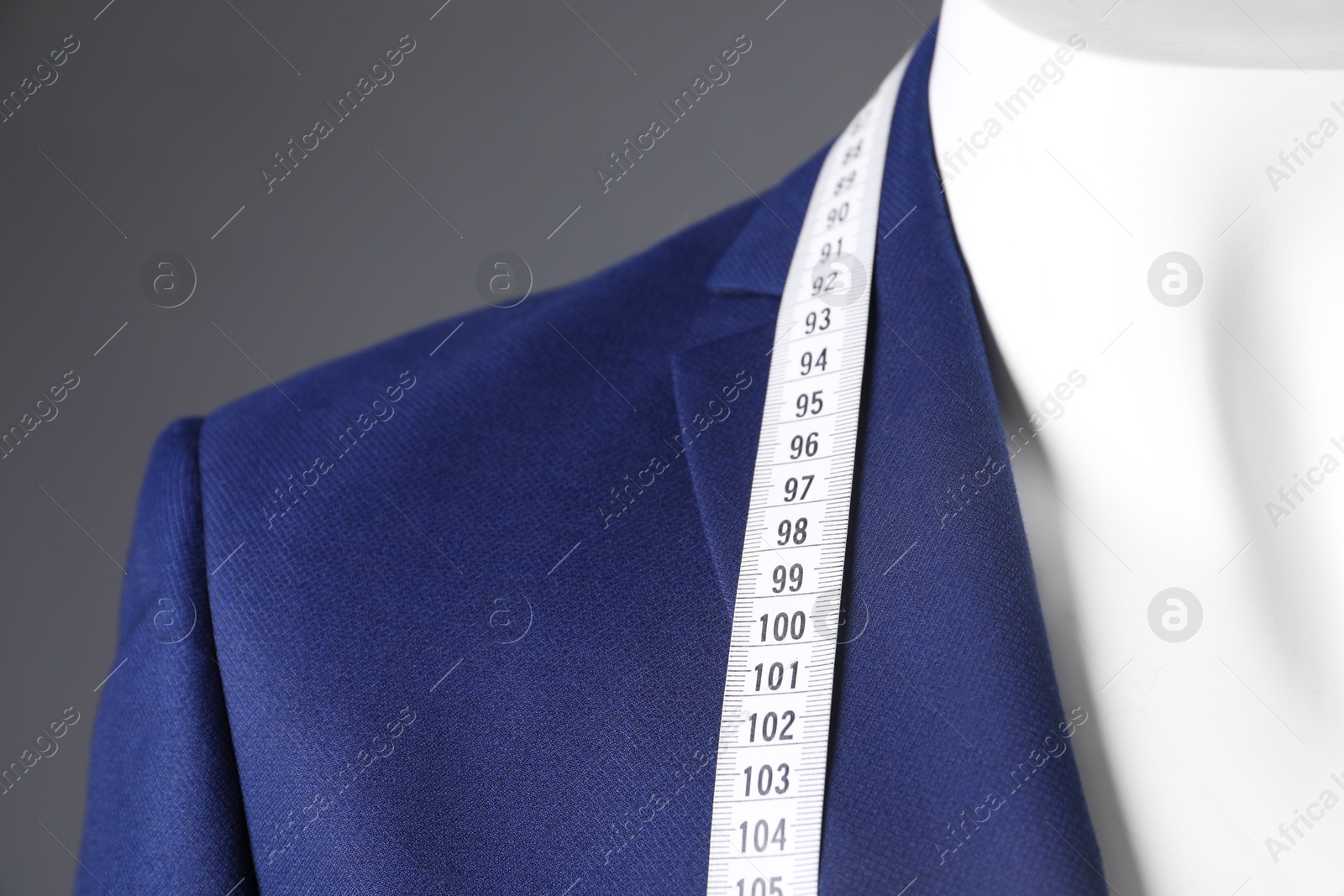 Photo of Mannequin with blue jacket and measuring tape on grey background, closeup