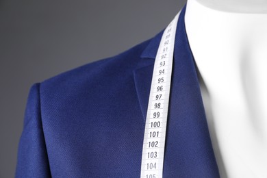 Photo of Mannequin with blue jacket and measuring tape on grey background, closeup