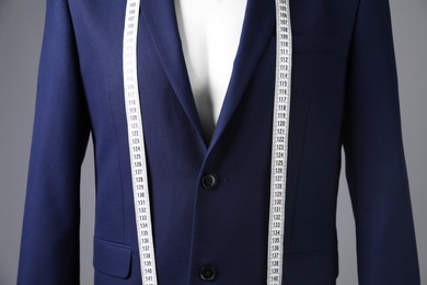 Male mannequin with blue jacket and measuring tape on grey background, closeup