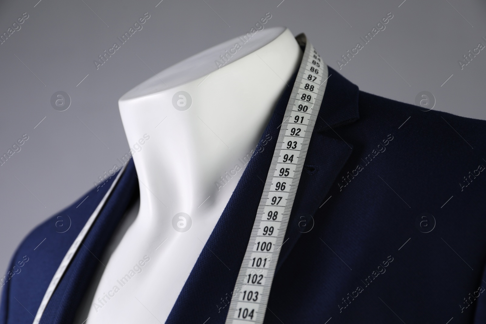 Photo of Male mannequin with blue jacket and measuring tape on grey background, closeup