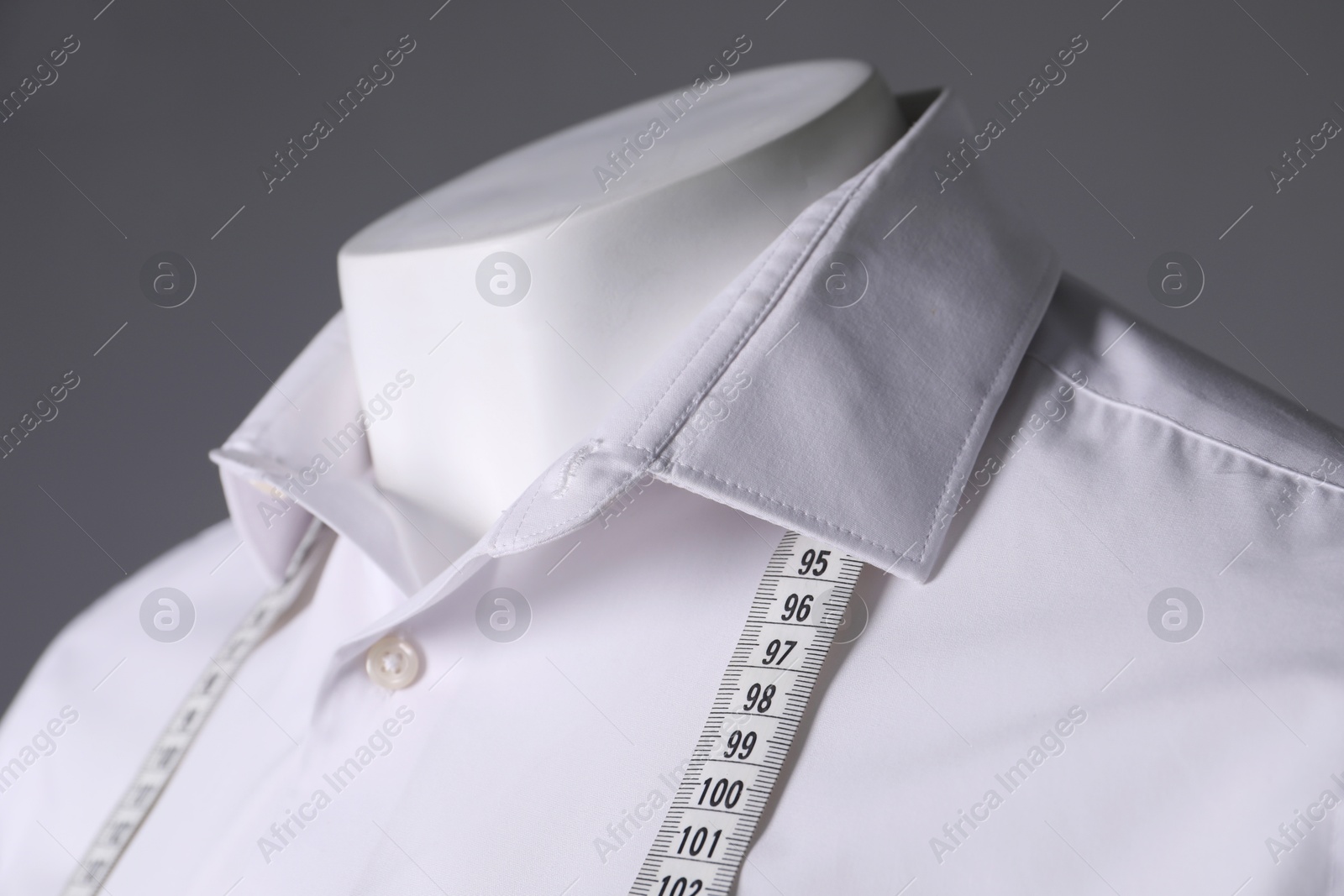 Photo of Male mannequin with white shirt and measuring tape on grey background, closeup