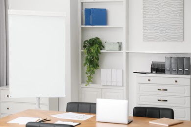 Photo of Flip chart, wooden table and chairs in conference room. Mockup for design