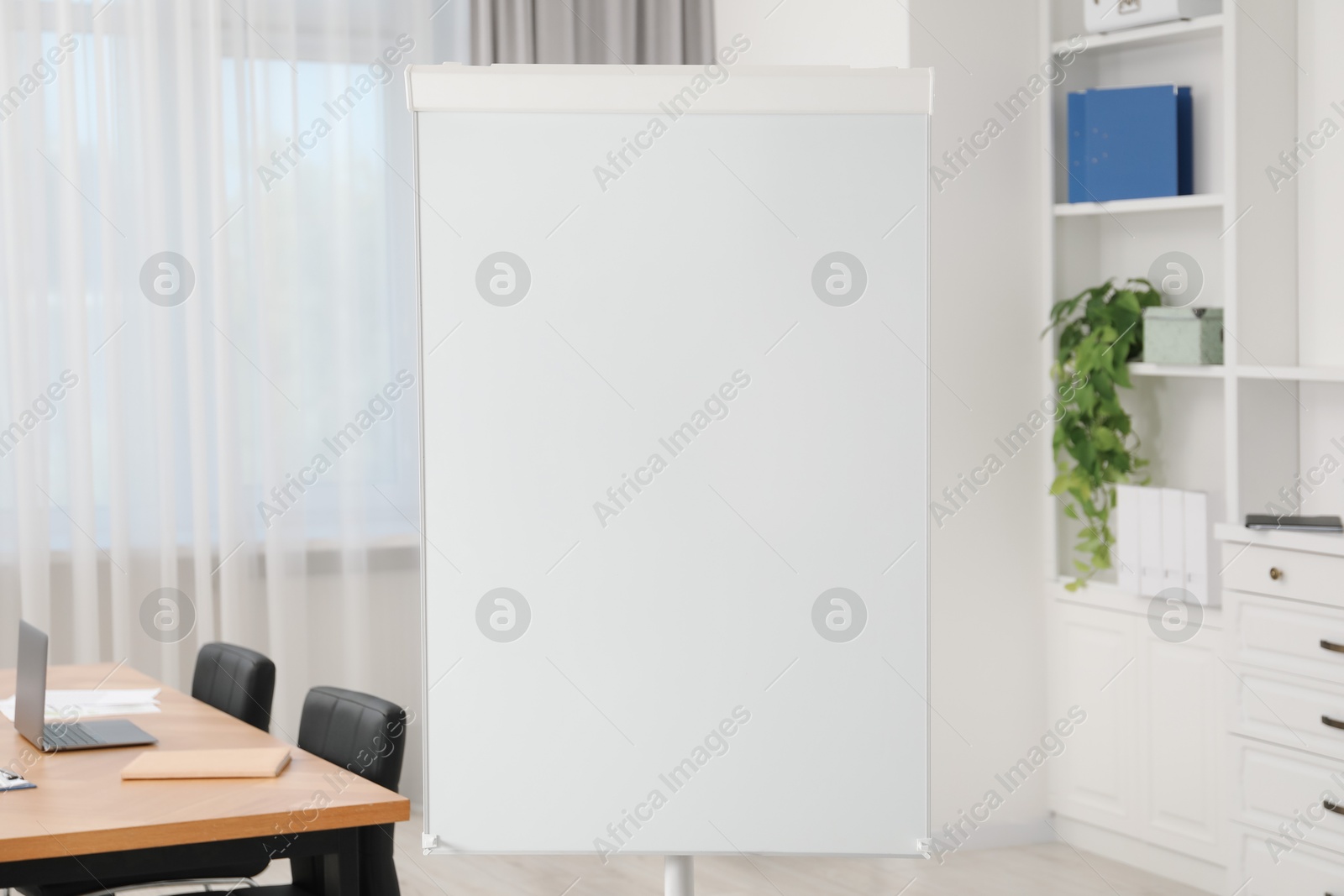 Photo of Flip chart, wooden table and chairs in conference room. Mockup for design