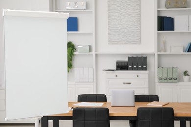 Photo of Flip chart, wooden table and chairs in conference room. Mockup for design