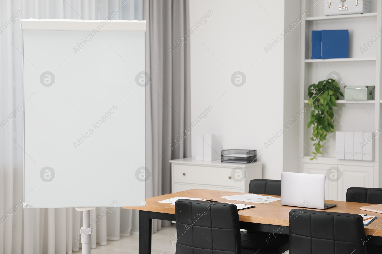 Photo of Flip chart, wooden table and chairs in conference room. Mockup for design