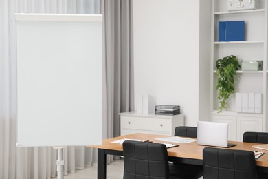 Photo of Flip chart, wooden table and chairs in conference room. Mockup for design