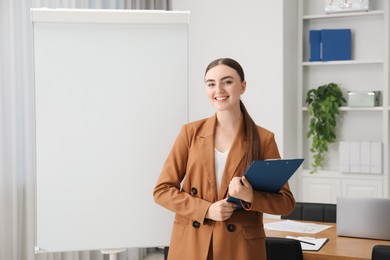 Photo of Happy woman with clipboard near flip chart in office. Mockup for design