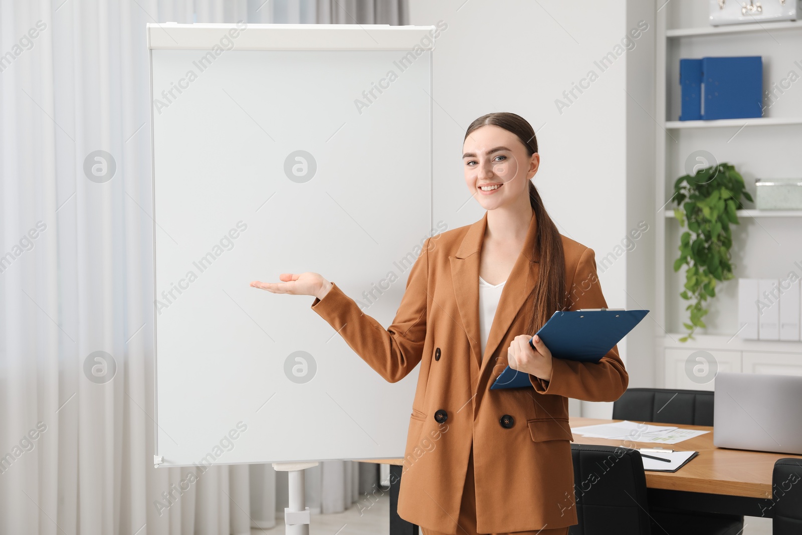 Photo of Happy woman with clipboard near flip chart in office. Mockup for design