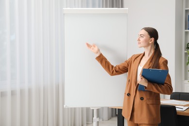 Photo of Woman with clipboard near flip chart in office. Mockup for design