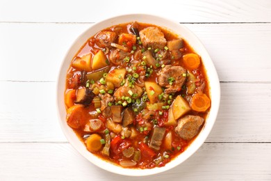 Photo of Delicious stew with vegetables in bowl on white wooden table, top view