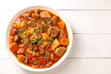 Photo of Delicious stew with vegetables in bowl on white wooden table, top view. Space for text