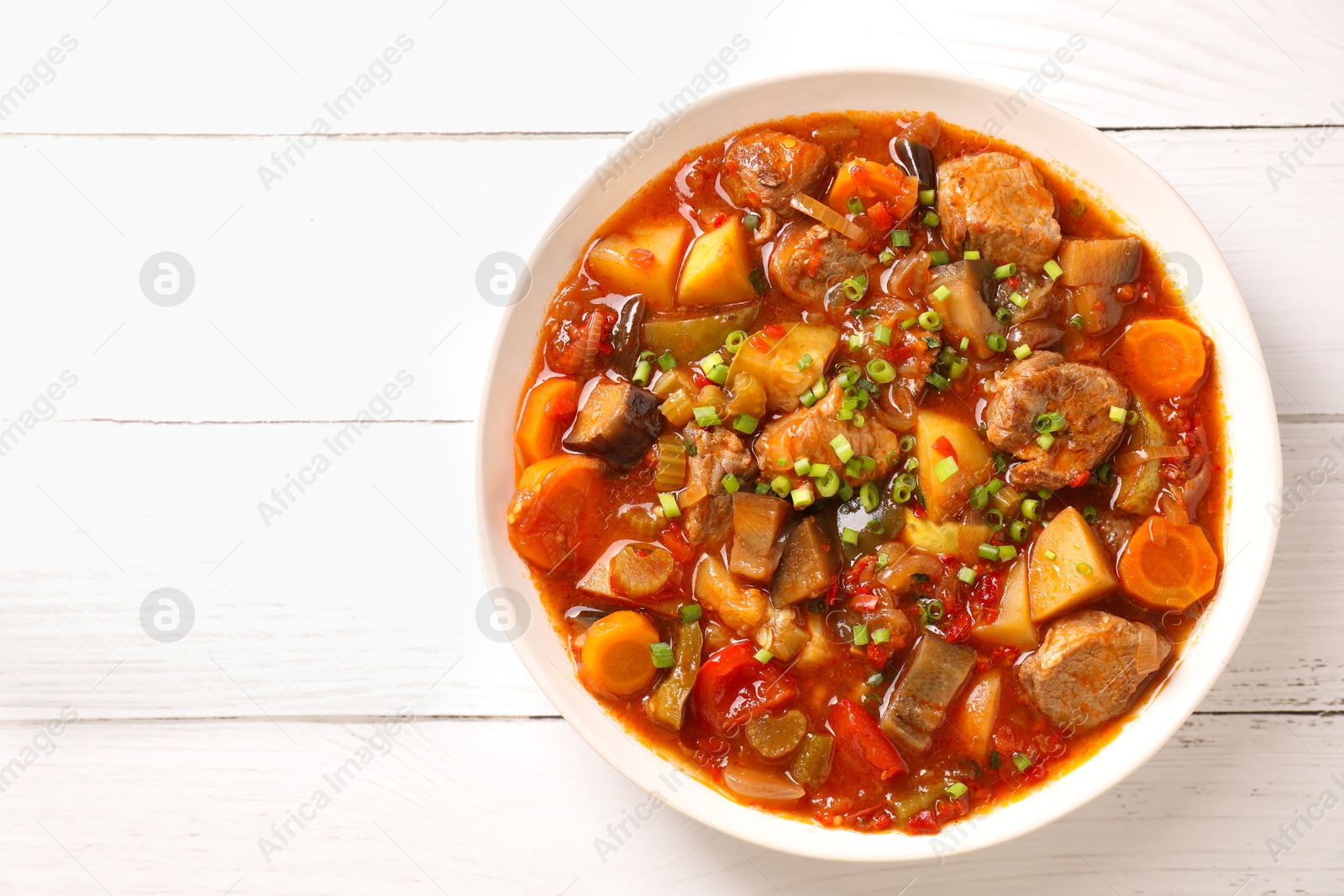 Photo of Delicious stew with vegetables in bowl on white wooden table, top view. Space for text