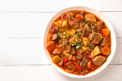 Delicious stew with vegetables in bowl on white wooden table, top view. Space for text