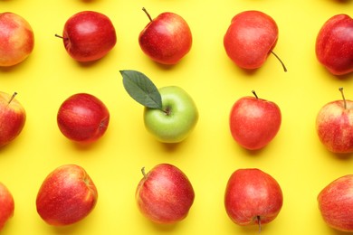 Photo of Flat lay composition with green apple surrounded by red ones on yellow background