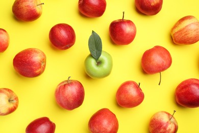 Flat lay composition with green apple surrounded by red ones on yellow background