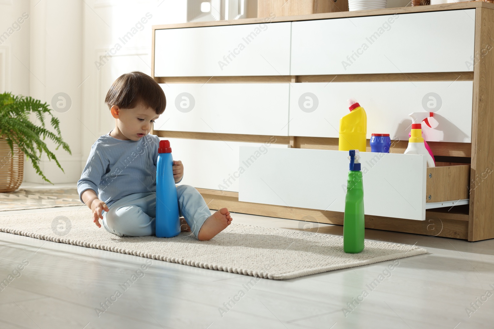 Photo of Little boy playing with bottles of detergents near cabinet at home. Child in danger