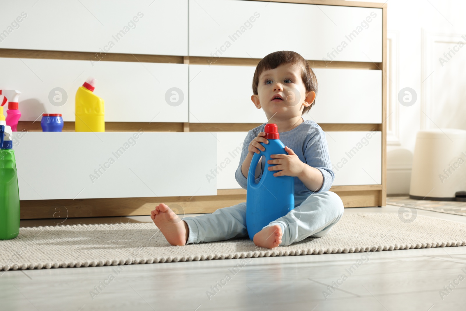 Photo of Little boy playing with bottles of detergents near cabinet at home. Child in danger