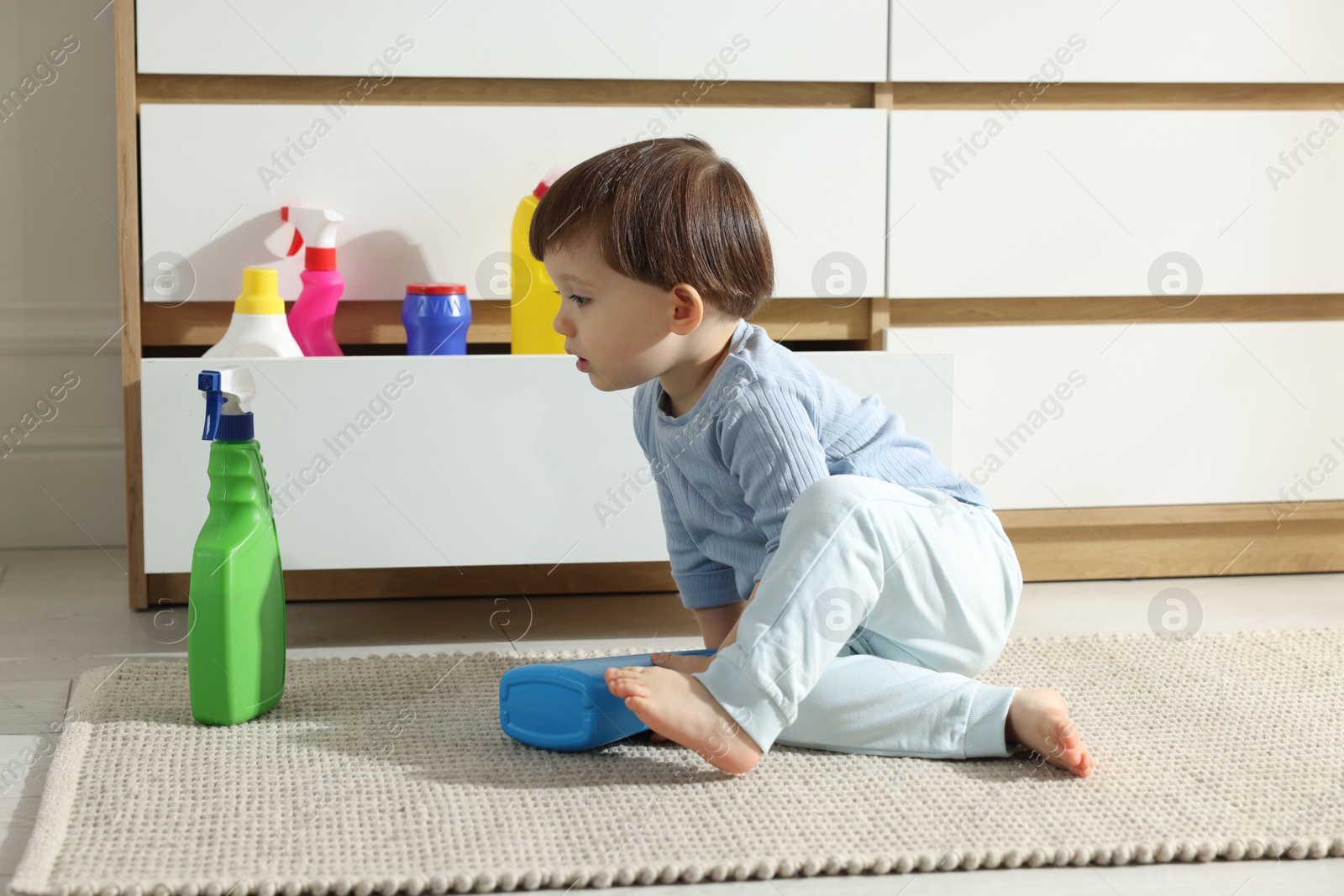 Photo of Little boy playing with bottles of detergents near cabinet at home. Child in danger