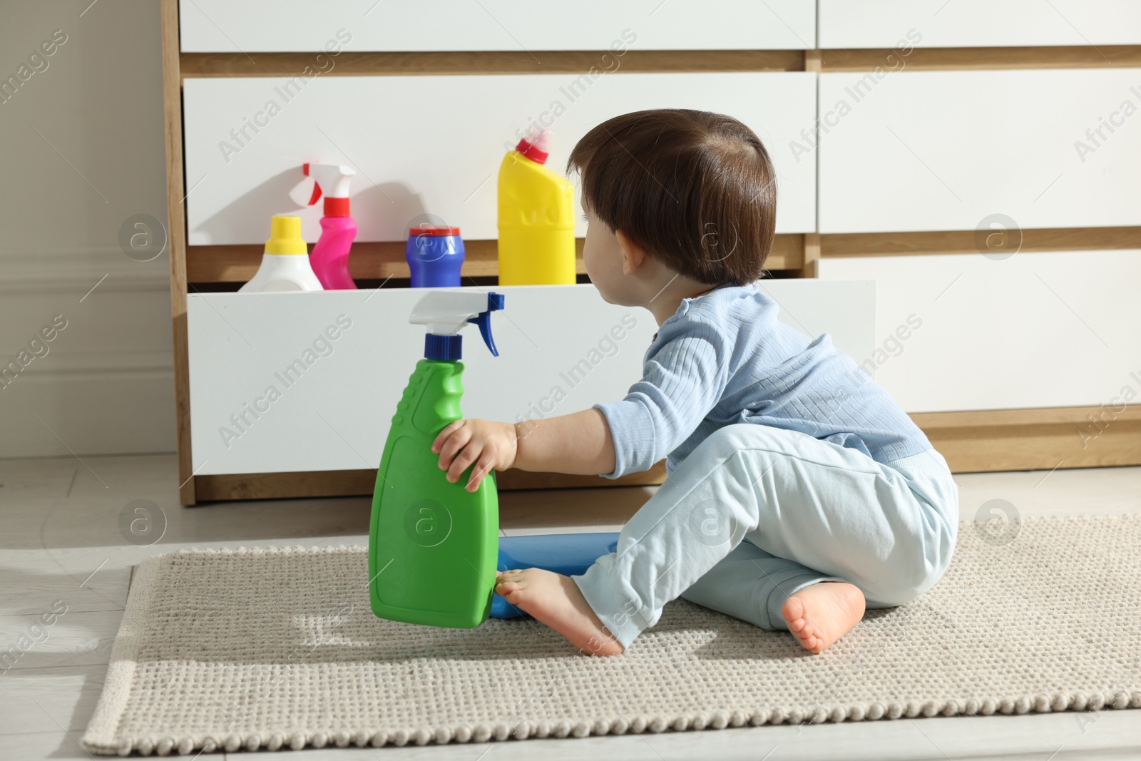 Photo of Little boy playing with bottles of detergents near cabinet at home. Child in danger