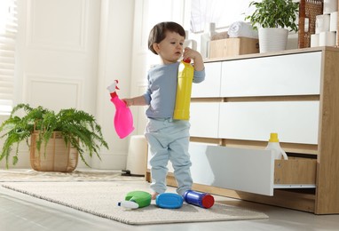 Photo of Little boy playing with bottles of detergents near cabinet at home. Child in danger