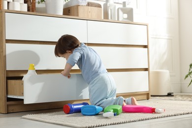 Photo of Little boy opening drawer with bottles of detergents at home, back view. Child in danger