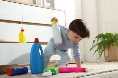 Photo of Little boy playing with bottles of detergents near cabinet at home. Child in danger