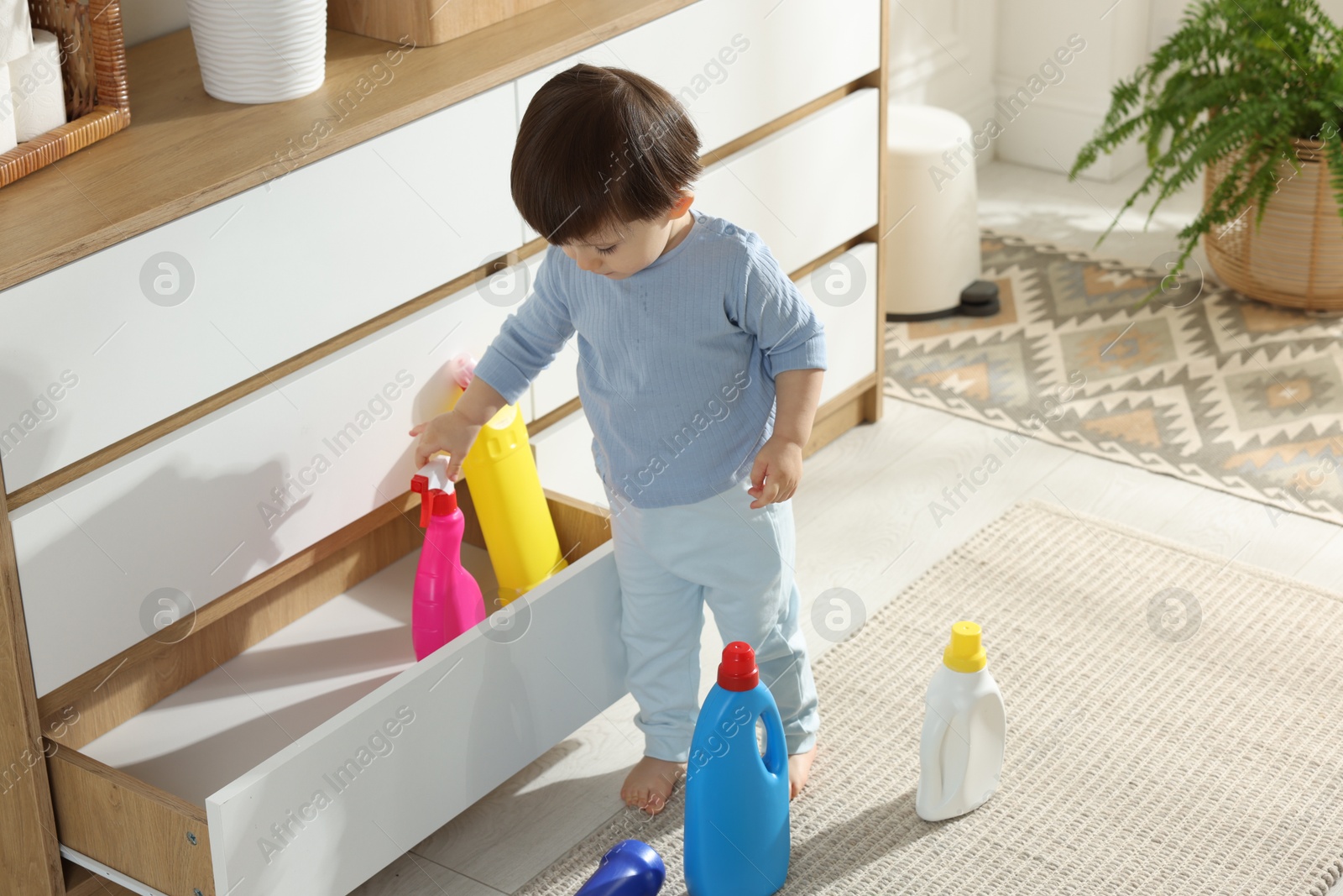 Photo of Little boy playing with bottles of detergents near cabinet at home. Child in danger