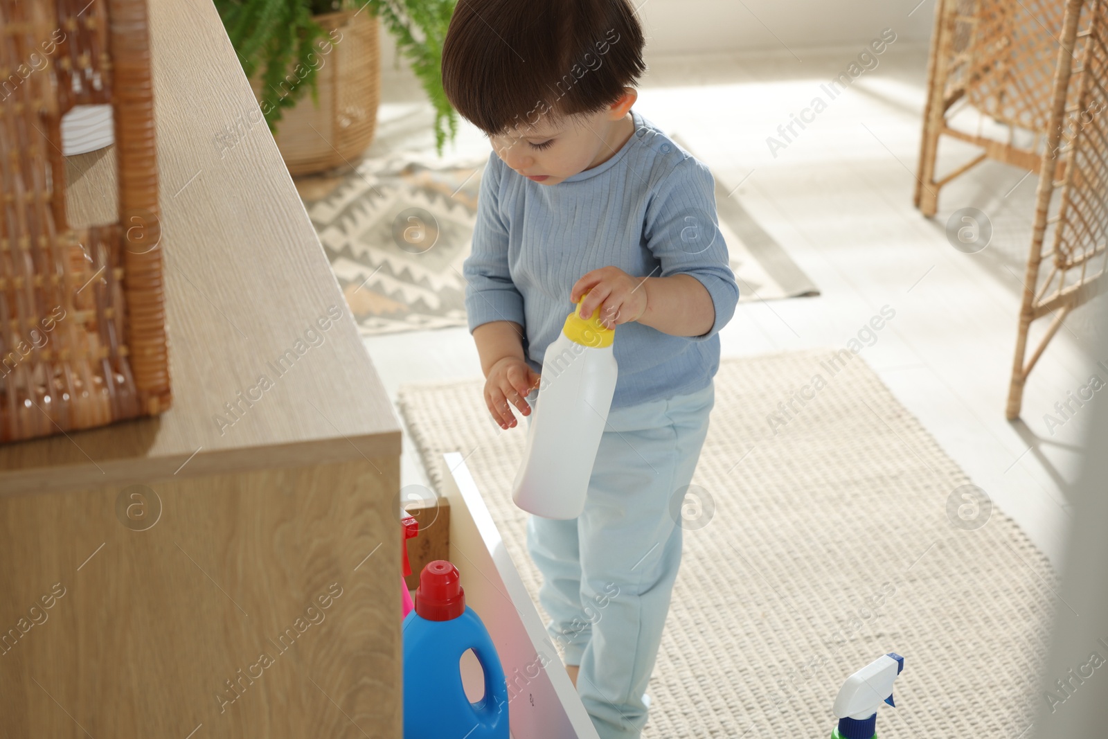 Photo of Little boy playing with bottles of detergents near cabinet at home. Child in danger