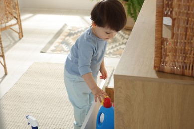 Photo of Little boy playing with bottles of detergents near cabinet at home. Child in danger