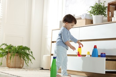 Photo of Little boy playing with bottles of detergents near cabinet at home, space for text. Child in danger