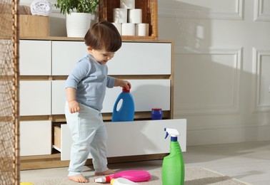 Photo of Little boy playing with bottle of detergent near cabinet at home, space for text. Child in danger