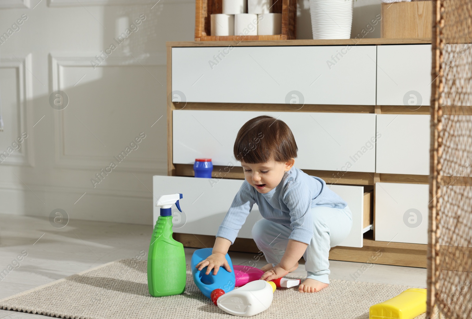 Photo of Little boy playing with bottles of detergents near cabinet at home, space for text. Child in danger