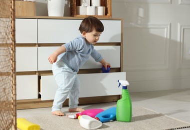 Photo of Little boy playing with bottles of detergents near cabinet at home, space for text. Child in danger