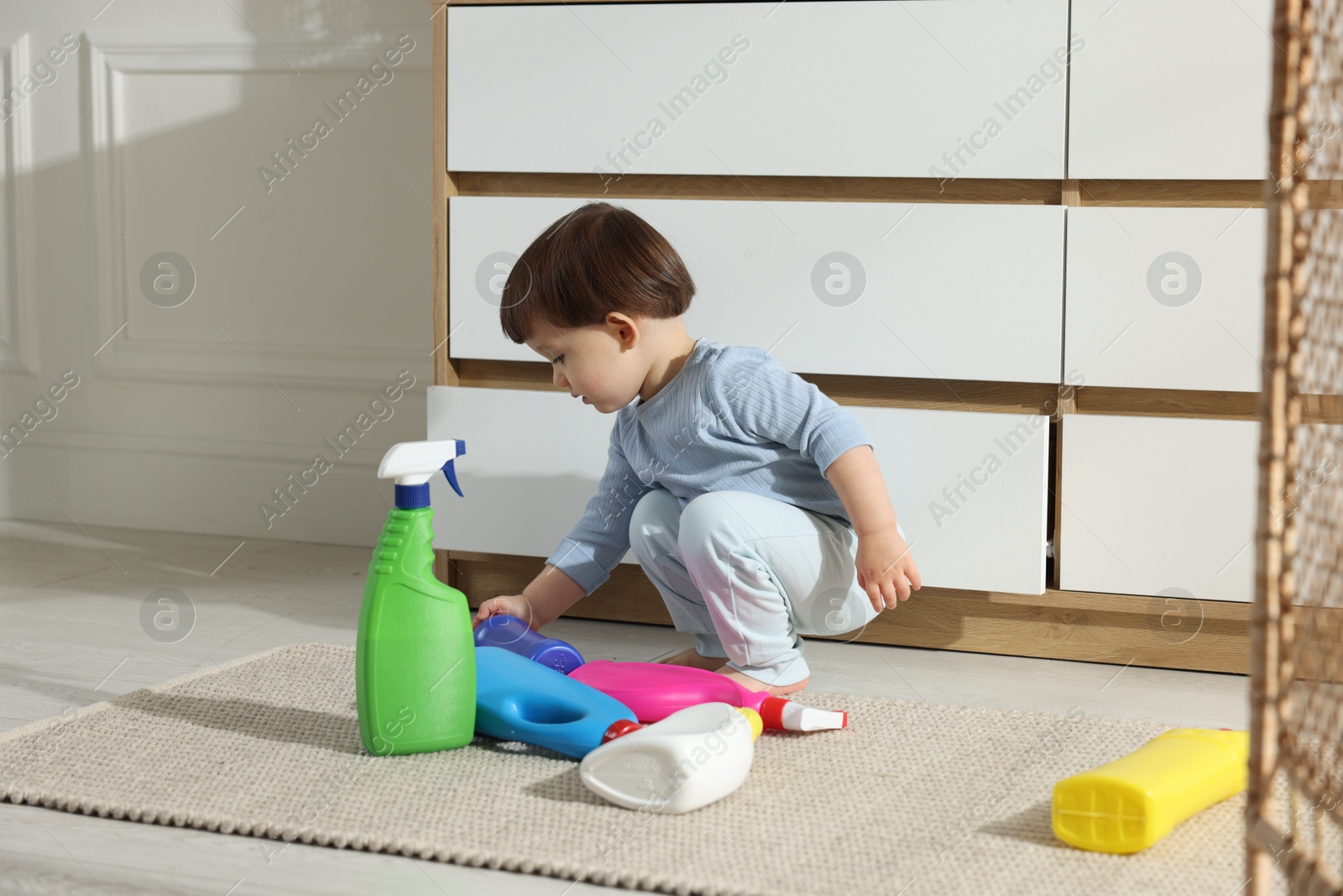 Photo of Little boy playing with bottles of detergents near cabinet at home. Child in danger