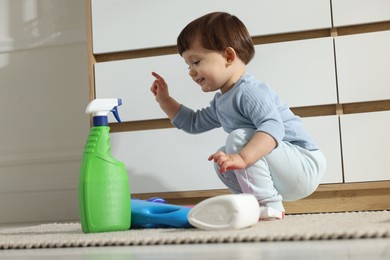 Photo of Little boy playing with bottles of detergents near cabinet at home. Child in danger