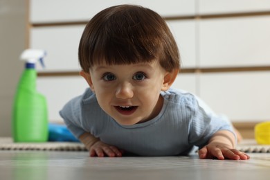 Photo of Little boy among bottles of detergents on floor at home. Child in danger