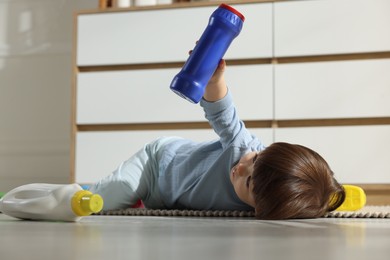 Photo of Little boy playing with bottles of detergents near cabinet at home. Child in danger