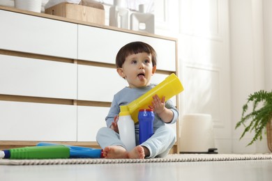 Photo of Little boy playing with bottles of detergents near cabinet at home. Child in danger