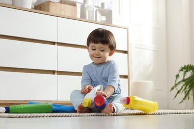 Photo of Little boy playing with bottles of detergents near cabinet at home. Child in danger