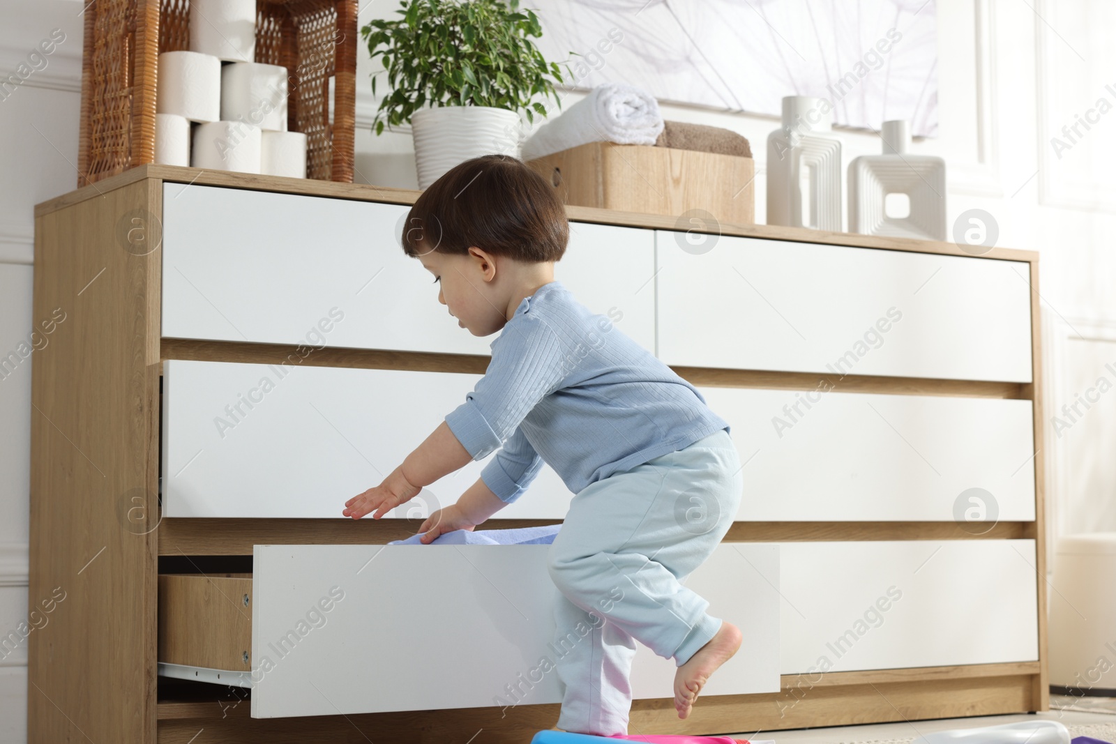 Photo of Little boy opening drawer with bottles of detergents at home. Child in danger