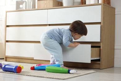 Photo of Little boy opening drawer with bottles of detergents at home. Child in danger