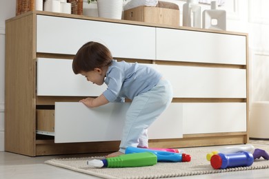 Photo of Little boy opening drawer with bottles of detergents at home. Child in danger