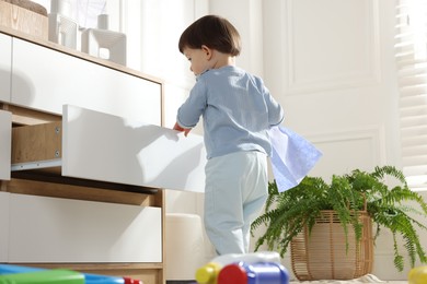 Photo of Little boy opening drawer with bottles of detergents at home, back view. Child in danger