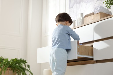 Photo of Little boy opening drawer at home, low angle view. Child in danger