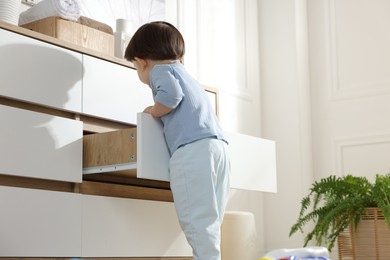 Little boy opening drawer at home, low angle view. Child in danger