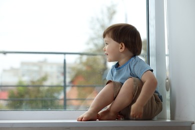 Photo of Little boy sitting on window sill, space for text. Child in danger