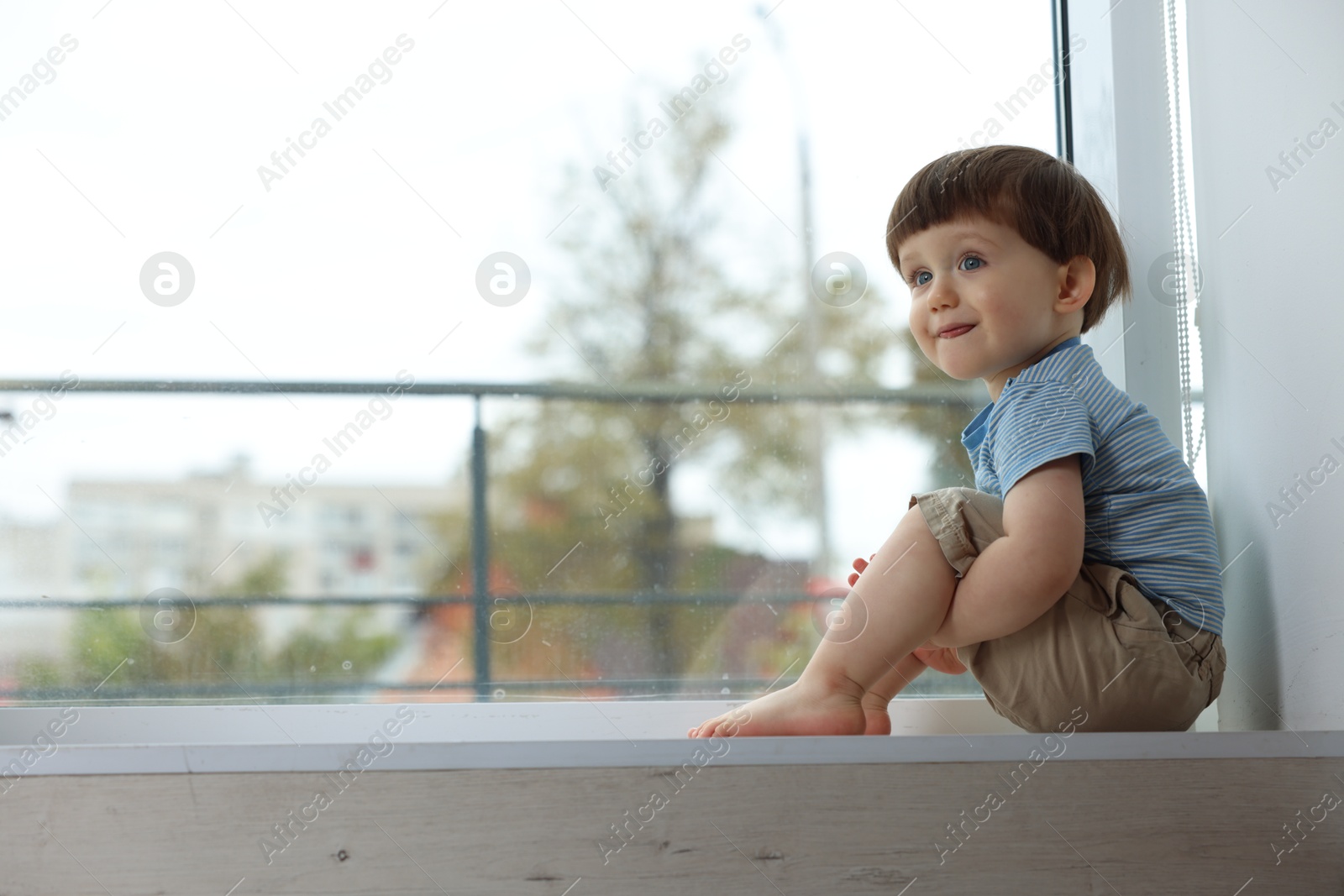 Photo of Little boy sitting on window sill, space for text. Child in danger